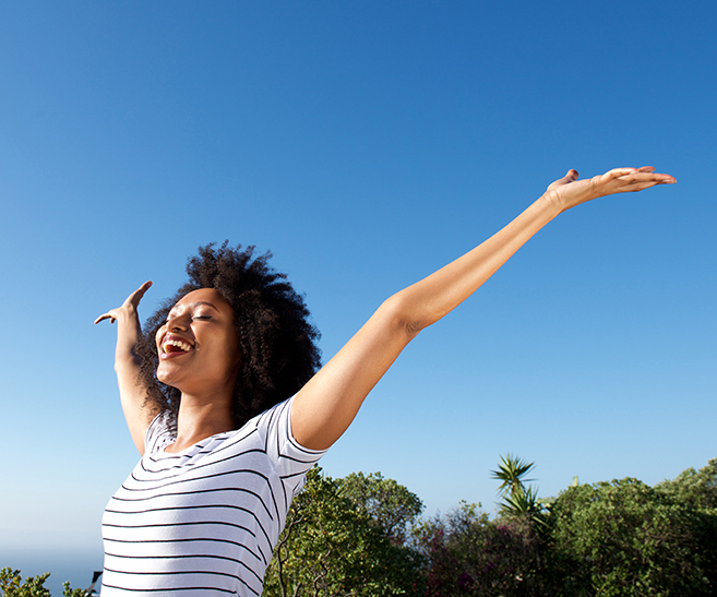 young african woman standing outdoors with arms raised and laughing Portrait of young african woman standing outdoors with arms raised and laughing